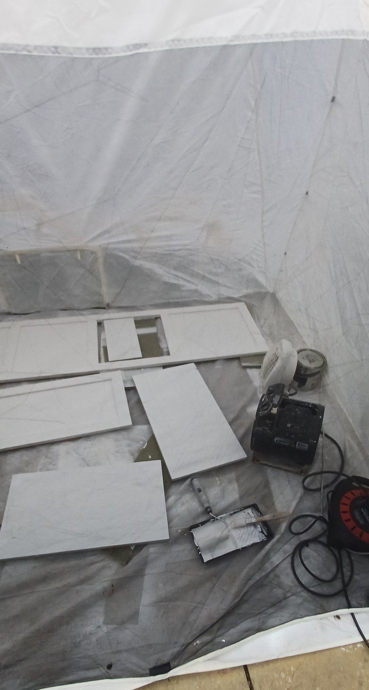 Kitchen doors off, flatted back and laid horizontal inside a polythene tent built on site.