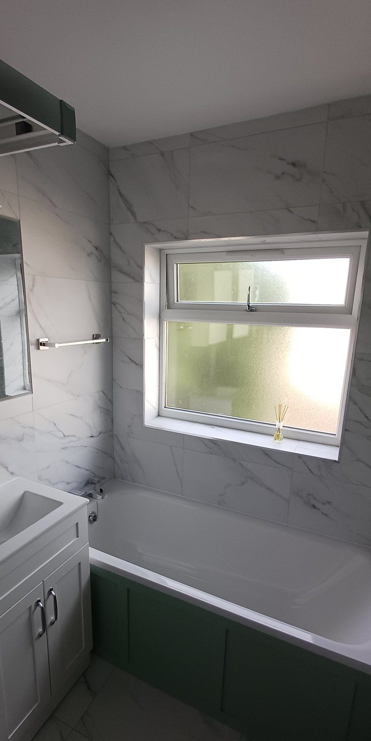 A finished bathroom in marble-effect tile with sage green panelling and heated towel rail.