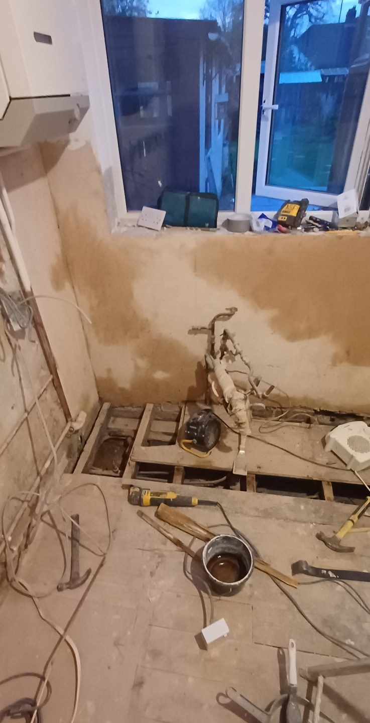 The same kind of room mid-job — tiles off, floor up, new waste and supply going in.