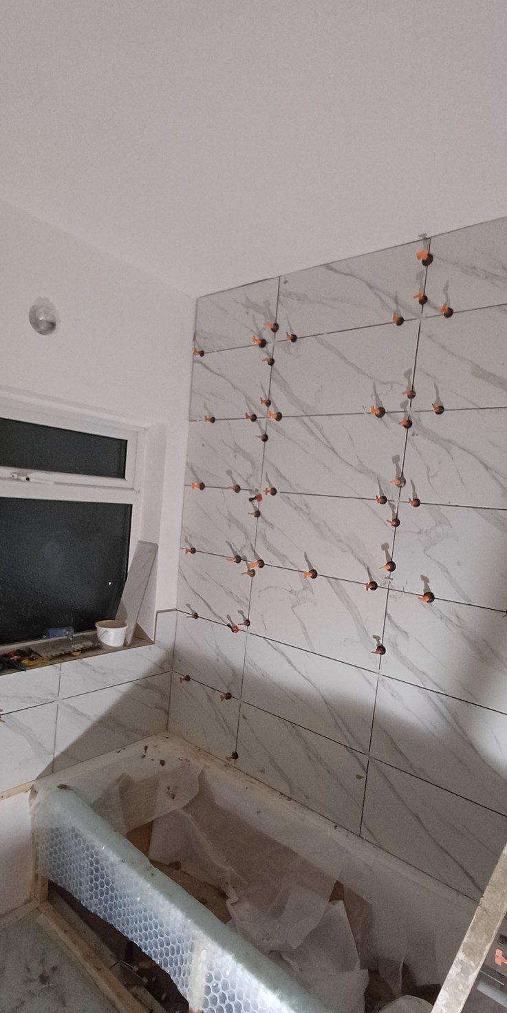 Marble-effect wall tiles going up with levelling clips throughout, so no edge stands proud in raking light.