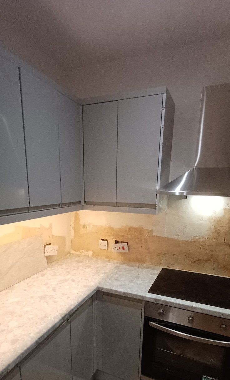 A grey handleless kitchen with marble-effect worktop, under-cabinet lighting and integrated oven.